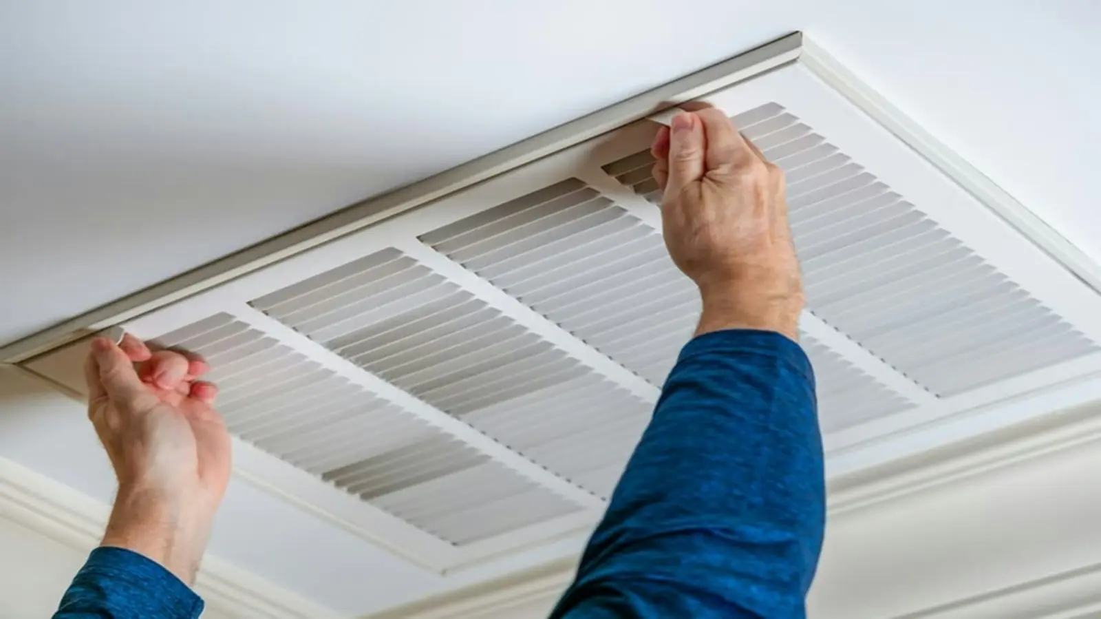 Technician removing a ceiling return-air grille before cleaning the duct behind it