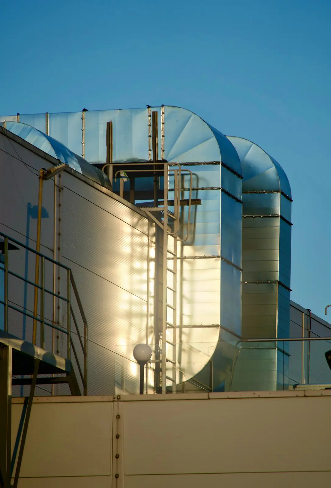 Galvanised ventilation ducts on a building rooftop against a blue sky